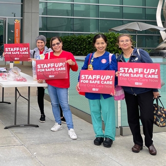 Group of nurses outside hospital holding signs "Staff Up for Safe Patient Care"