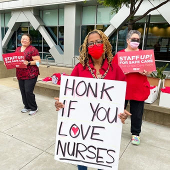 Nurse outside hospital holds sign "Honk in you love nurses"
